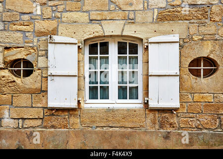 Fenêtre avec volets blancs dans un bâtiment en pierre avec deux petites fenêtres de chaque côté à Saint-Robert, Corrèze, Limousin, France. Banque D'Images