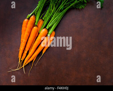 Tas de matières premières fraîches carottes orange avec des feuilles vertes bush sur planche à découper en bois Banque D'Images