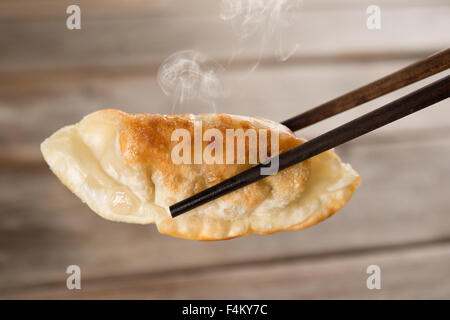 Close up fresh dumpling frit avec des baguettes. La nourriture chinoise avec la vapeur chaude sur fond de bois vintage rustique. Banque D'Images