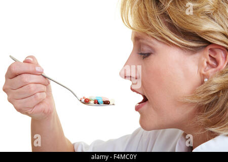 Femme mangeant une cuillère pleine de pilules colorées Banque D'Images