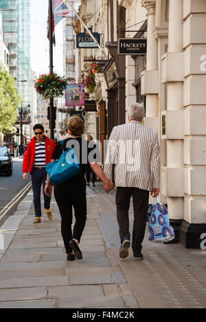 Mature couple walking le long de Jermyn Street à Londres, se tenant la main et shopping dans les mêmes tons de bleu. Banque D'Images
