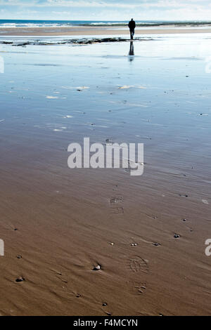Homme marchant le long de la plage, laissant des traces de pas dans le sable. Northumberland, Angleterre Banque D'Images
