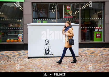 Cours de marche des piétons street art, peinture, décoration murale graffiti. Baby sitting sur Casque de policier ; style Banksy art de rue Birley, UK Banque D'Images