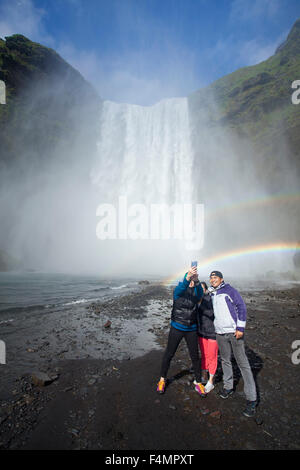 Les touristes dans l'arc-en-ciel en dessous de 60m de haut, la cascade Skogafoss, Skogar, Sudhurland, Islande. Banque D'Images