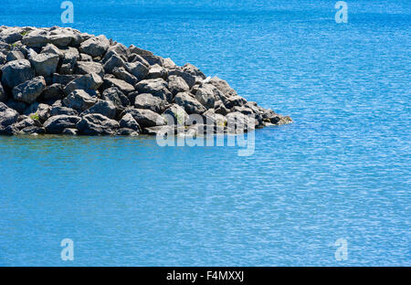 Bord du mur rocheux qui descend dans l'eau peu profonde avec des ondulations dans cyan léger vent. Banque D'Images