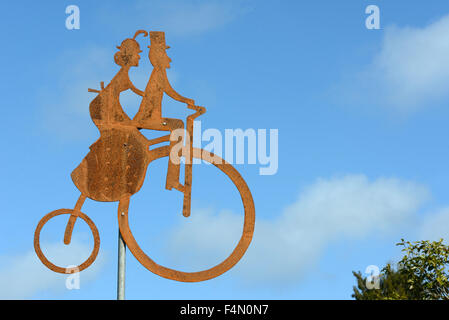 Rusty silhouette of a man and woman riding a penny farthing location Banque D'Images