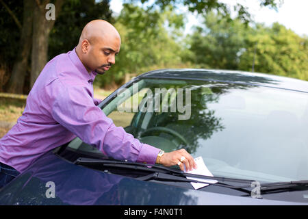 Jeune homme de laisser un message sur un pare-brise de voiture Banque D'Images