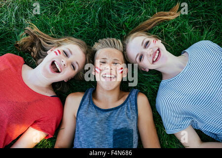 L'Autriche, trois adolescents avec les couleurs peintes sur leurs joues allongé sur un pré Banque D'Images
