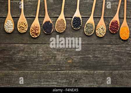 Diverses légumineuses séchées dans des cuillères en bois sur l'ancienne table Banque D'Images