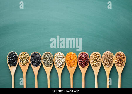 Diverses légumineuses séchées dans des cuillères en bois sur green chalkboard Banque D'Images