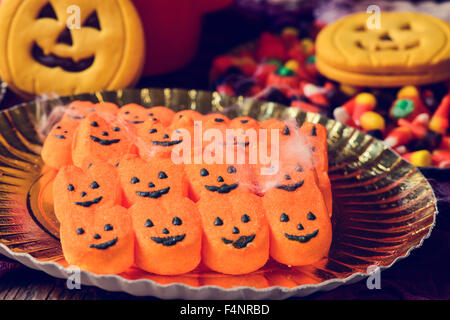 Quelques bonbons en forme de citrouille dans un bac d'or sur une table et d'autres bonbons et biscuits dans l'arrière-plan Banque D'Images