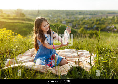 Petite fille assise sur un lit et tenant une bouteille d'eau Banque D'Images