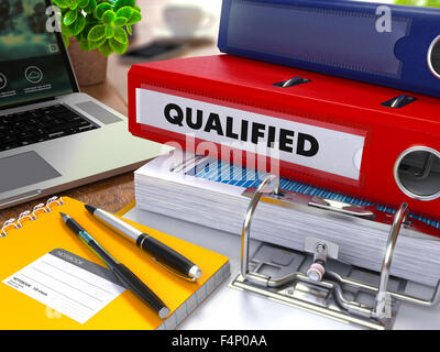 Classeur rouge avec l'inscription qualifié sur la table de travail de fond avec les fournitures de bureau, ordinateur portable, des rapports. Tonique Illustrat Banque D'Images