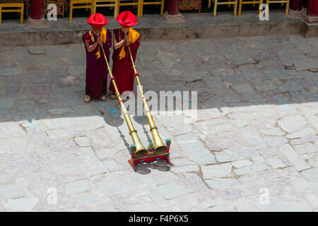 Deux moines avec des vêtements rouges sont l'ouverture du festival hemis dans la cour du monastère en soufflant de grandes cornes Banque D'Images