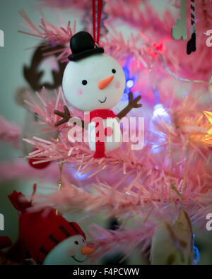 Décoration d'arbre de Noël Bonhomme de neige souriant très heureux avec bras accroché à un arbre rose avec des lumières Banque D'Images