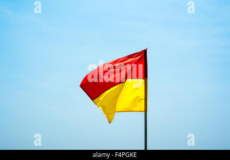 La plage rouge et jaune de la sécurité de l'eau ciel pâle contre drapeau, palpitations dans le vent. Banque D'Images