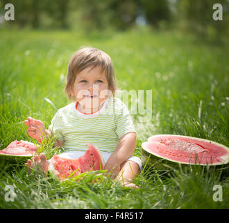 Heureux l'enfant avec de grandes tranche de pastèque rouge assis sur l'herbe verte. Concept de saine alimentation Banque D'Images