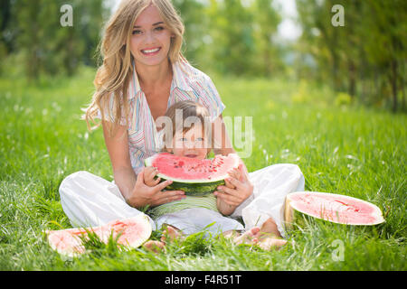 Heureuse maman et son eating watermelon on Green grass Banque D'Images