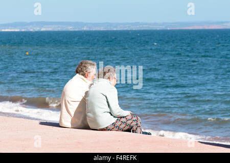 Deux dames âgées sitting on steps au plage Oddicombe profitant de la vue, de Torbay sur chaude journée à Torquay, Devon, Angleterre Banque D'Images