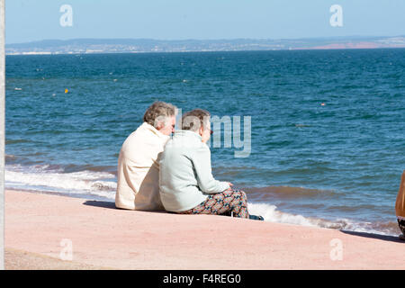 Deux dames âgées sitting on steps au plage Oddicombe profitant de la vue, de Torbay sur chaude journée à Torquay, Devon, Angleterre Banque D'Images