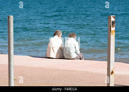 Deux dames âgées sitting on steps au plage Oddicombe profitant de la vue, de Torbay sur chaude journée à Torquay, Devon, Angleterre Banque D'Images