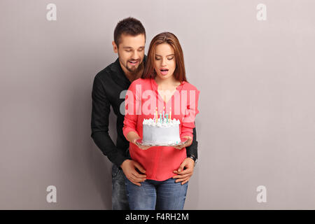 Young Girl holding a surpris un gâteau d'anniversaire et son petit ami l'étreindre de derrière Banque D'Images