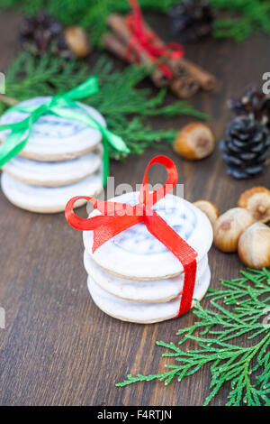 Les biscuits de Noël avec des rubans, pommes, noix, pommes de pin, la cannelle et le thuya vert direction sur une table en bois. Banque D'Images