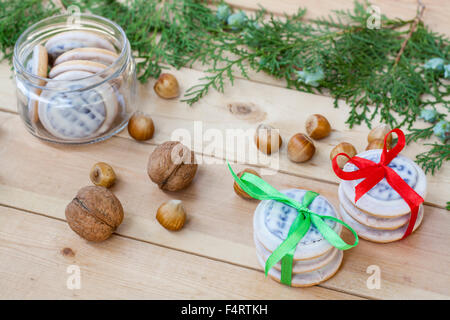 Les biscuits de Noël avec des rubans, pommes, noix, pommes de pin, la cannelle et le thuya vert direction sur une table en bois. Banque D'Images