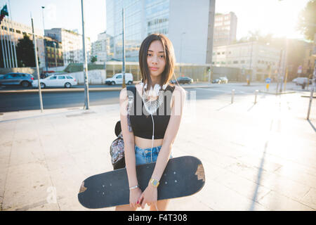 La figure du genou de jeunes asiatiques beau brun long cheveux droits femme écoute patineur de la musique avec des écouteurs, à la caméra en souriant, - sportive, de la musique, de bonheur, de détente concept Banque D'Images