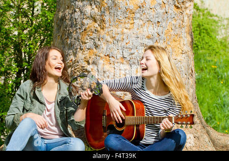 Deux filles assis dans le parc et faire de la musique Banque D'Images