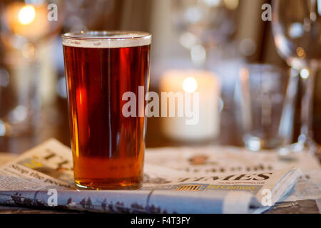 Une pinte de bière sur une table de pub avec des journaux Banque D'Images