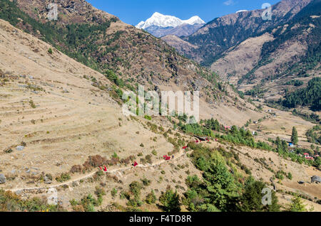 Moines et moniales portant des chiffons rouges marche sur un petit sentier le long d'une pente de montagne Banque D'Images