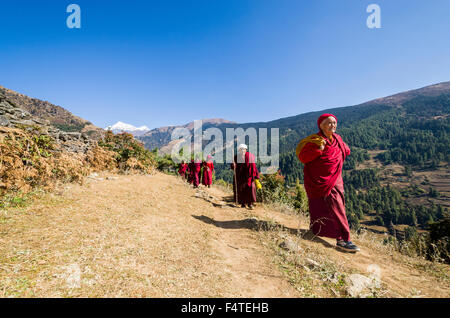 Moines et moniales portant des chiffons rouges marche sur un petit sentier le long d'une pente de montagne Banque D'Images