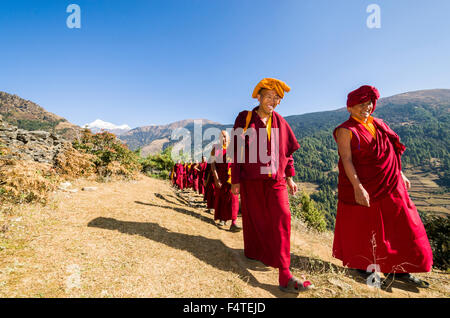 Moines et moniales portant des chiffons rouges marche sur un petit sentier le long d'une pente de montagne Banque D'Images