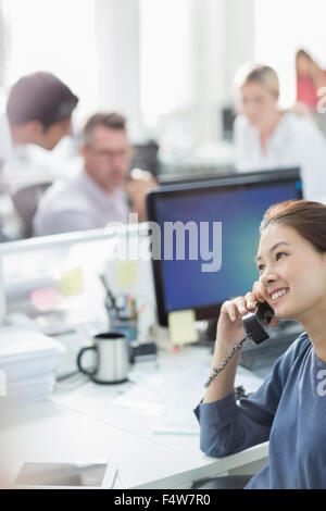 Smiling businesswoman talking on telephone at desk in office Banque D'Images