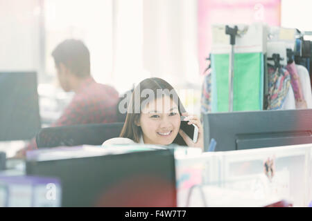 Smiling Fashion designer talking on cell phone at desk in office Banque D'Images