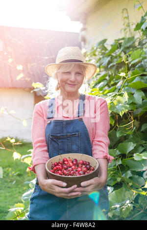 Portrait of smiling woman holding en salopette cerises récoltées Banque D'Images