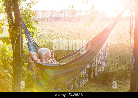 Serene woman sieste dans un hamac à côté de champ de blé rural ensoleillé Banque D'Images