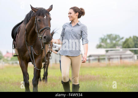 Smiling woman walking horse in rural pasture Banque D'Images