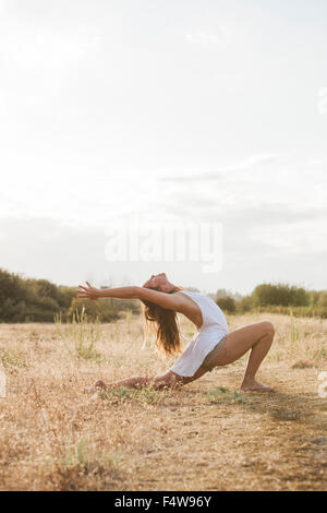 Boho femme en haute fente en croissant yoga pose à sunny rural field Banque D'Images