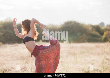 Boho femme en danseuse king yoga pose à sunny rural field Banque D'Images