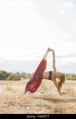 Boho femme en longue planche latérale yoga pose à sunny rural field Banque D'Images