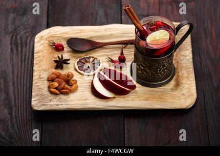 Hot Toddy (vin chaud, punch) avec des pommes et cynorrhodons servi sur plateau en bois rustique avec des amandes sur table en bois foncé Banque D'Images