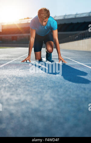 Athlète masculin professionnel en position sur le sprint de blocs d'une piste de course dans le stade d'athlétisme. Banque D'Images