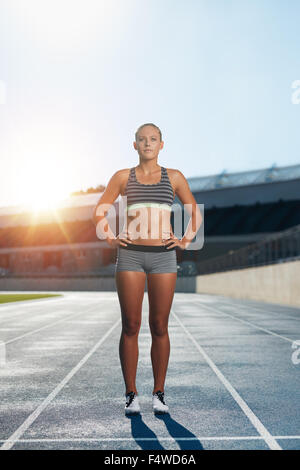 Coup de pleine longueur athlète féminine professionnelle comité permanent avec ses mains sur les hanches à la caméra en toute confiance à. Runner sur la race tr Banque D'Images