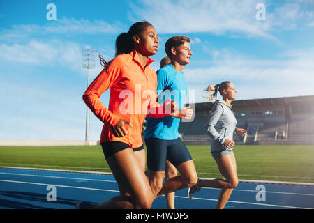 Groupe de coureurs s'exécutant sur la piste de course dans le stade. Les jeunes athlètes masculins et féminins pratiquant ensemble sur des courses. Banque D'Images