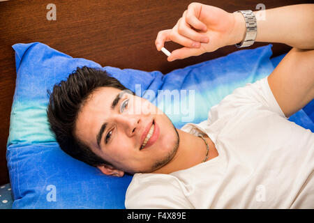 Jeune homme séduisant au lit en prenant un médicament en comprimé ou comprimé Banque D'Images