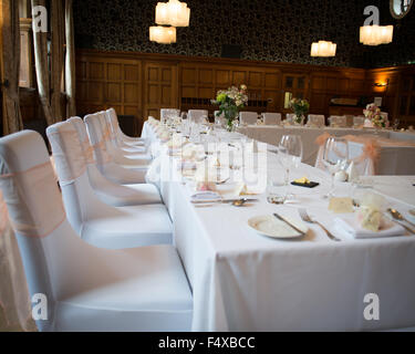 Réception de Mariage table top table avec nappes blanches et pêche Housses de chaises fixées avec des plaques d'usure de couverts en argent Banque D'Images
