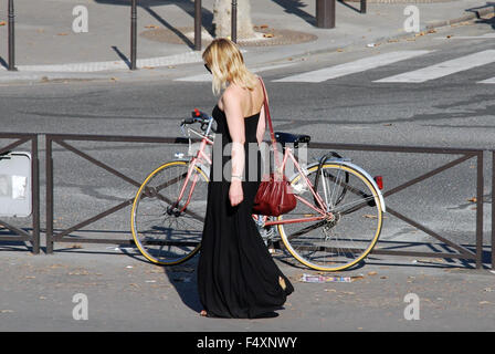 Femme portant robe maxi longue marche à travers la rue à côté de vélo Rose à Paris, France. Banque D'Images