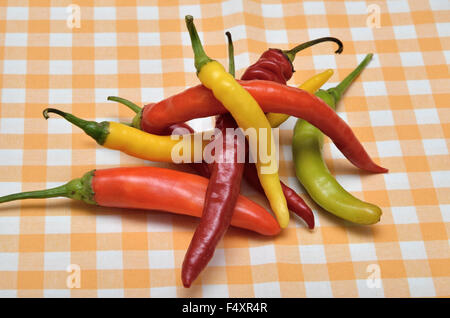 Pile de rouge, orange, vert et jaune hot chili peppers sur nappe jaune-blanc Banque D'Images